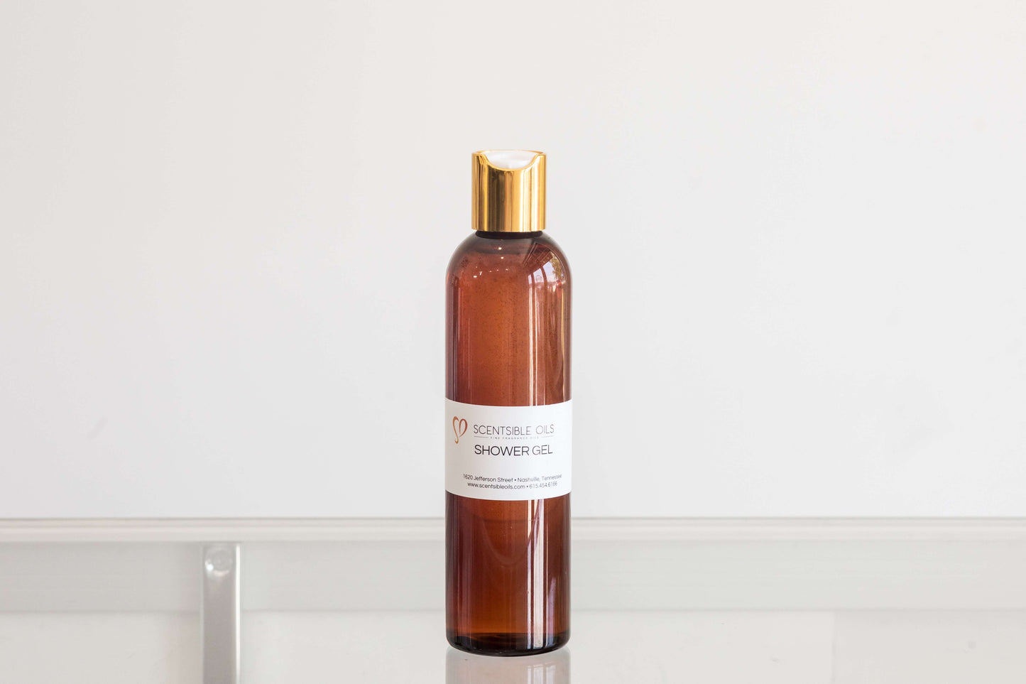 Men Shower Gel in an amber bottle with a gold cap on a minimalistic background.