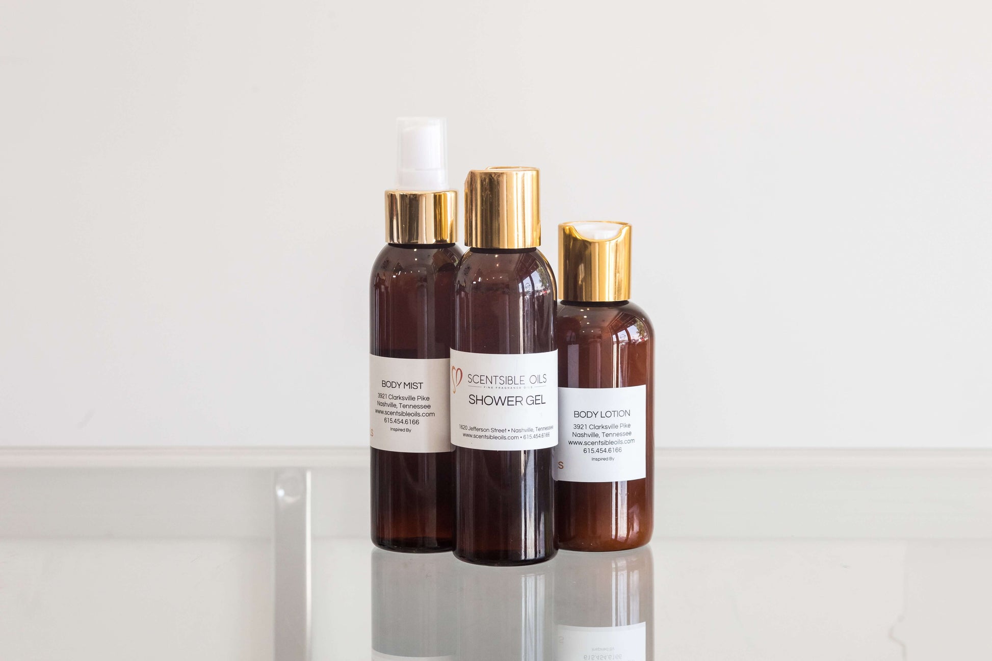 Women Body Mist and shower gel bottles with gold caps on a glass surface.